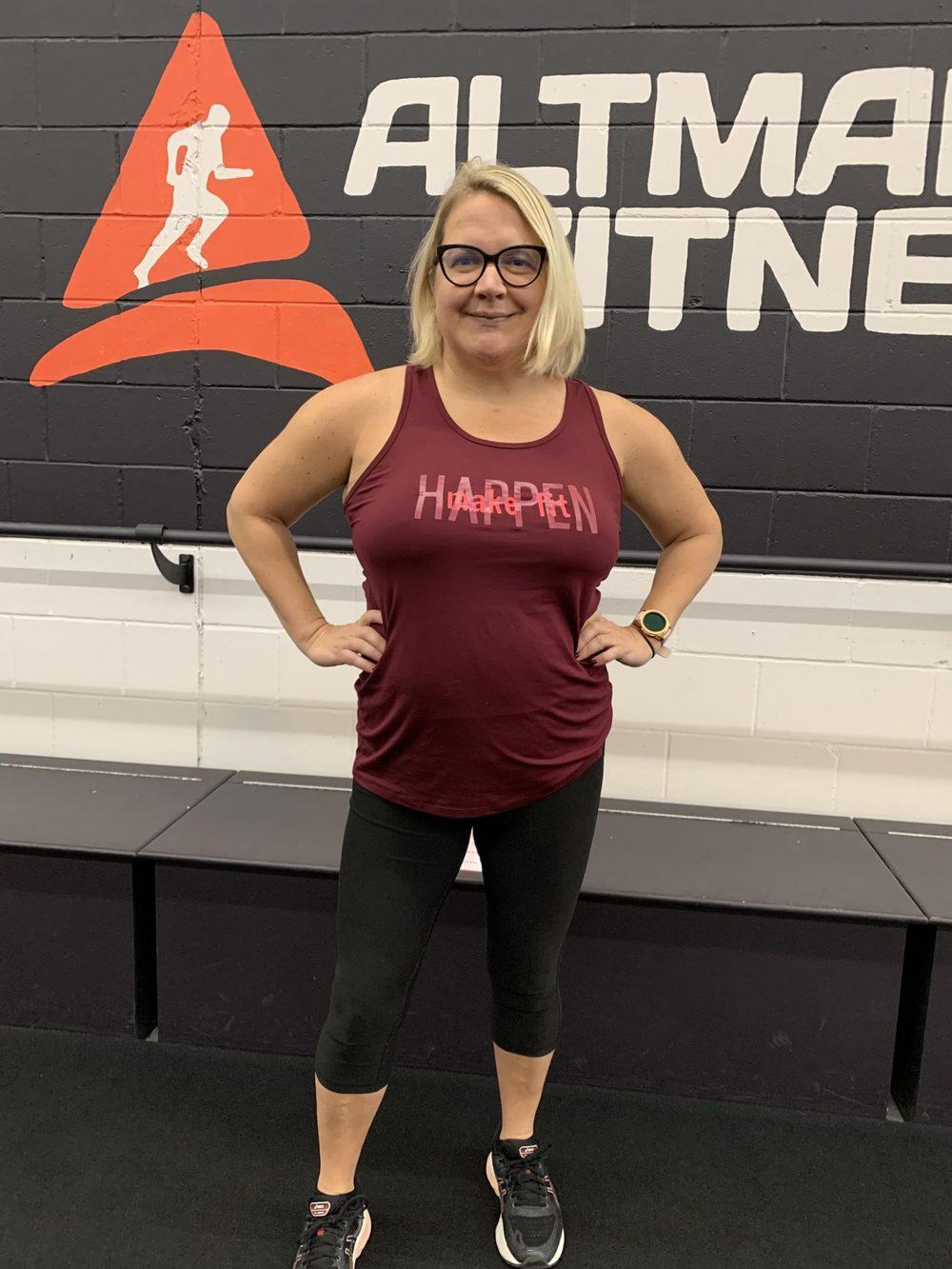 A member celebrating a milestone in front of the Altman Fitness wall
